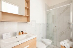 Ein modernes Badezimmer mit Marmorwaschbecken, Toilette, Bidet und einer Duschkabine.