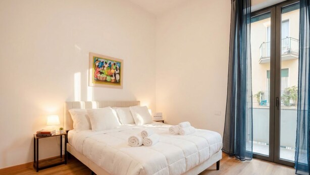 Un dormitorio con cama, mesita de noche, un cuadro en la pared y vistas al exterior.