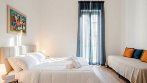 Habitación de hotel con cama, mesita de noche, lámpara, ventana con cortinas y un cuadro en la pared.