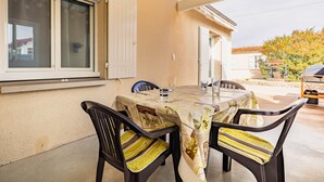 Un portico coperto con tavolo e sedie, una finestra con persiane e vista su una zona residenziale.