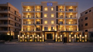 Een meerlaags hotel met een centrale ingang, balkons op elke verdieping, en een logo boven de ingang.