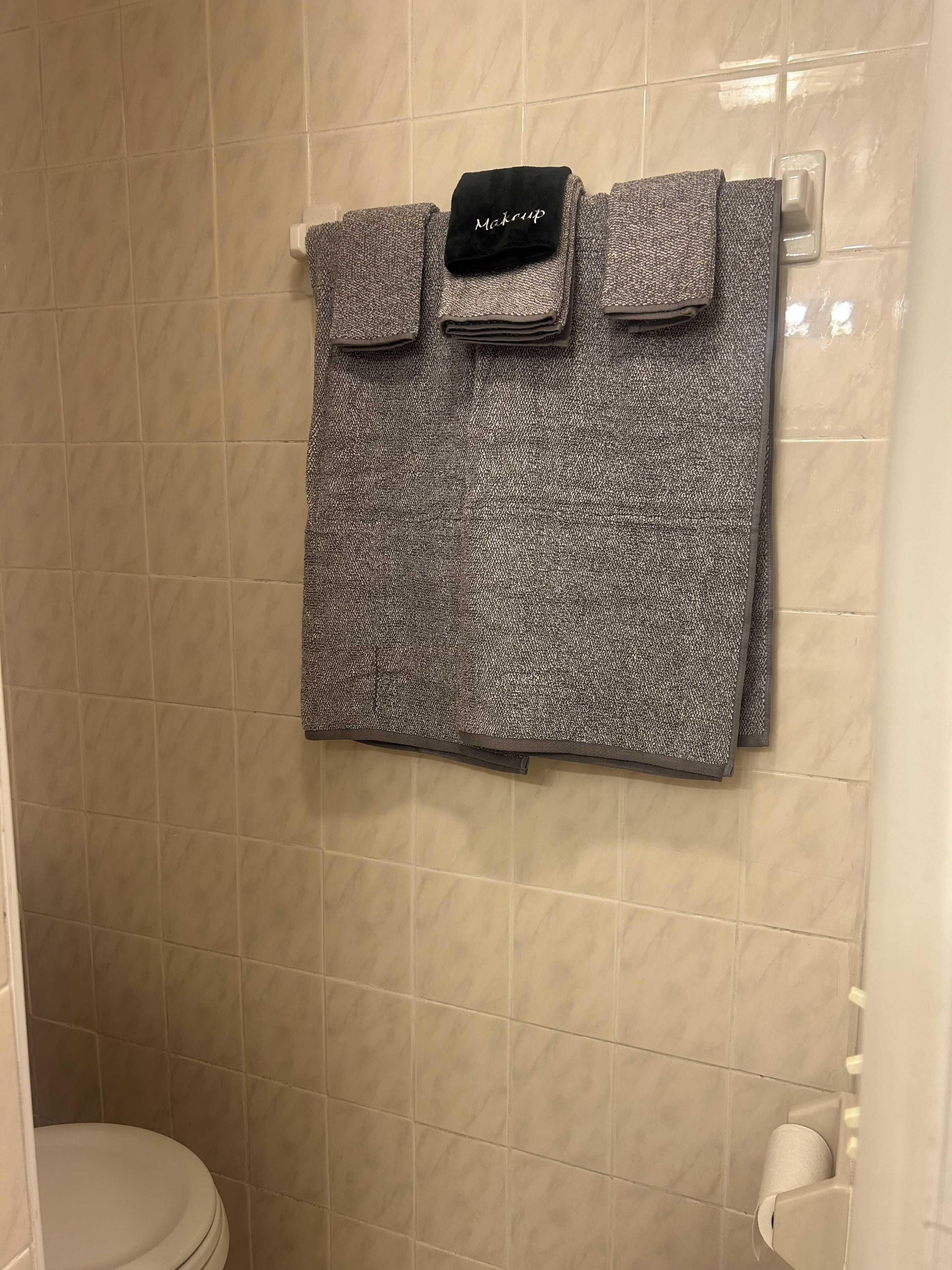 A bathroom with beige tiled walls, a white toilet, and a towel rack with a folded towel and a black towel with "McLoughlin" on it.