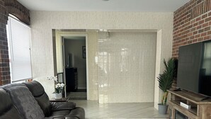 Una sala de estar con un sofá de cuero oscuro, un tapete estampado, un televisor sobre un mueble de madera y una pared de ladrillo.