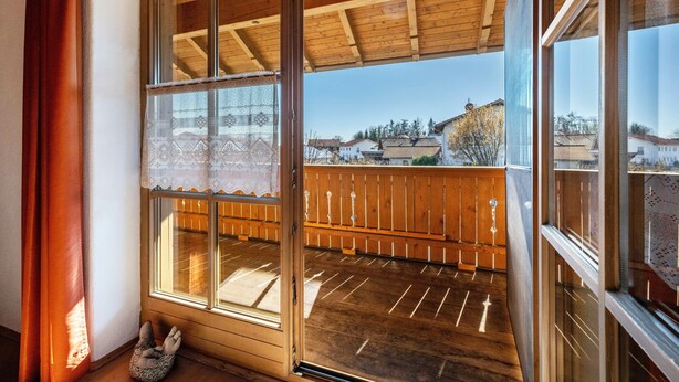 A balcony with wooden railings, a lace curtain, and a view of buildings in the distance. - Apartment 'Gassner' with Balcony and Wi-Fi (Fridolfing)