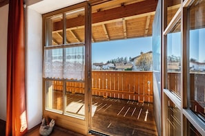 A balcony with wooden railings, a lace curtain, and a view of buildings in the distance. - Apartment 'Gassner' with Balcony and Wi-Fi (Fridolfing)