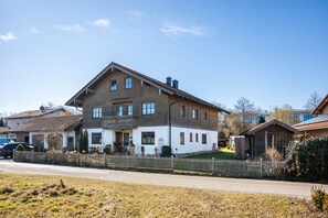 A two-story house with a balcony, a fenced yard, and a clear sky. - Apartment 'Gassner' with Balcony and Wi-Fi (Fridolfing)