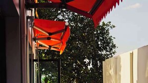 An outdoor seating area with tables and chairs, a red umbrella, and a view of trees and a building in the background. - ATOUR Rayong Hotel (Pluak Daeng)