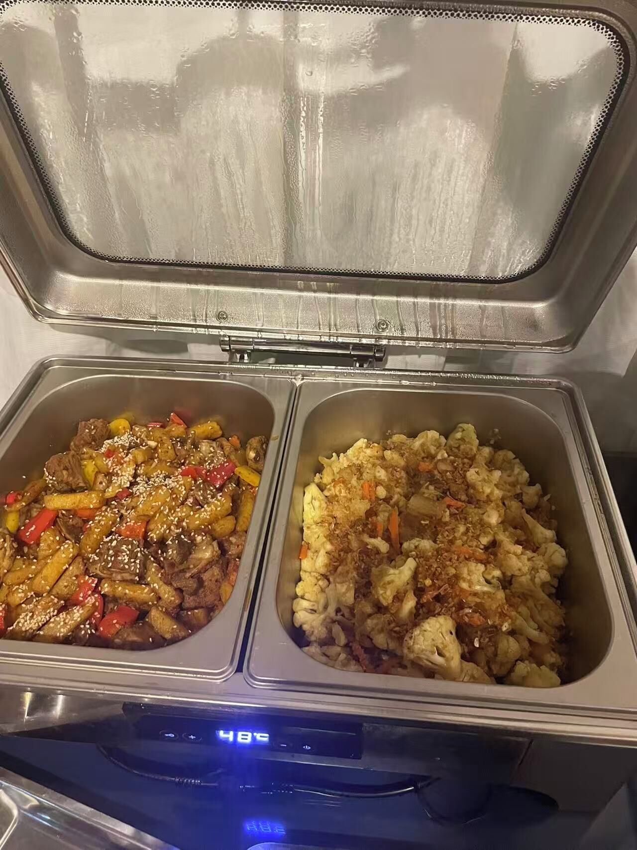 A food service area with two stainless steel containers, one with a stir-fry dish and the other with a rice dish.