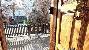 Una puerta de madera con un picaporte y un aldabón de latón, que da a un espacio exterior nevado con una cerca de madera y un felpudo.