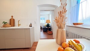 Una cocina con encimera de madera, un fregadero y un florero con plantas secas. Hay un cuenco de fruta en el alféizar de la ventana.