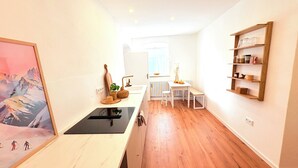 Una cocina con encimera de madera, un fregadero y un ventanal. Hay una estantería con utensilios de cocina y un cuadro en la pared.