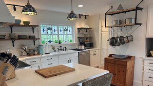 A kitchen with a central island, white cabinetry, a wooden chair, and hanging pots. - Stunning 3-bedroom Weskeag Village River House in South Thomaston (South Thomaston)