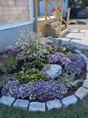A garden with a wooden staircase, various flowering plants, and a stone border.