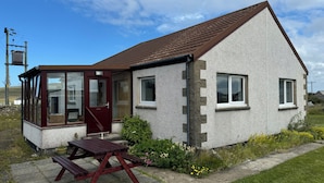 A single-story house with a conservatory, a wooden bench, and a small garden area.