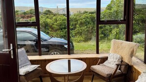 A cozy seating area with a wooden ceiling, large windows offering a view of the countryside, and a car parked outside.