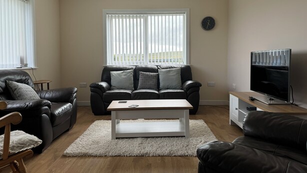 A living room with a sofa, a coffee table, a TV, and a window with blinds.