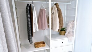 Ein weißer Kleiderschrank mit Kleidung, ein pinkfarbener Tüllrock, ein flauschiger Mantel und ein Korbwäscheschale.