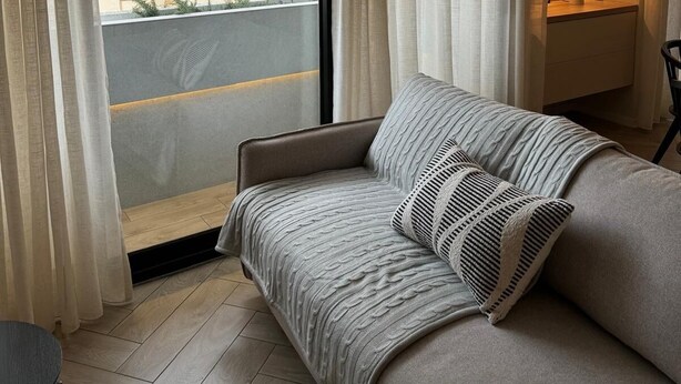 Ein gemütliches Zimmer mit einer Couch, einem kleinen Tisch und einem Fenster mit Vorhängen.