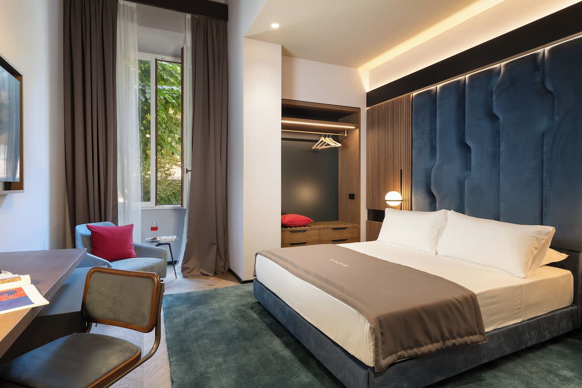 Een moderne hotelkamer met een groot bed, een bureau met stoel, een bijzettafeltje en een kledingkast.