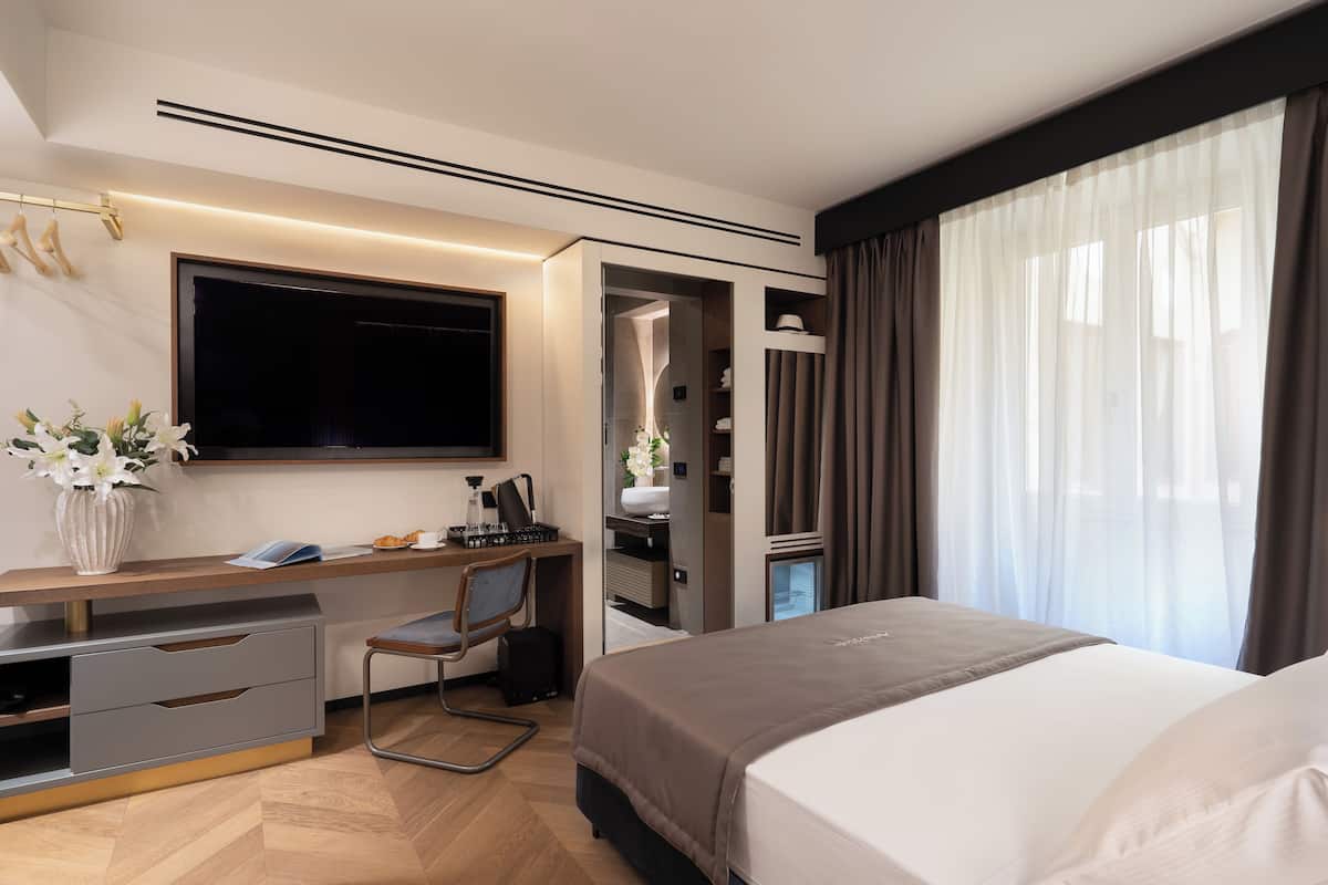 Een moderne hotelkamer met een bed, bureau, stoel en een groot raam met gordijnen.