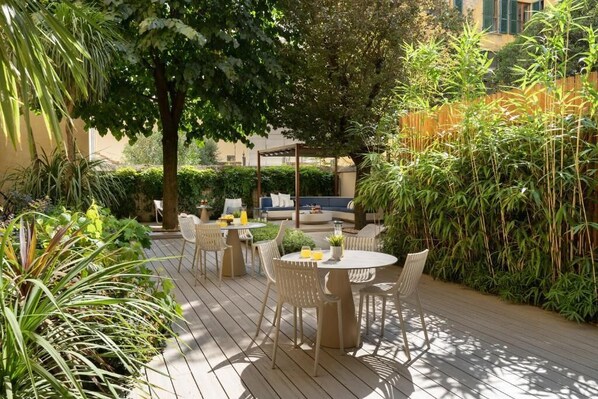 An outdoor patio with a round table and chairs, surrounded by lush greenery and a bamboo fence. - Arts & Crafts Luxury Suites by Amalia (Florence)