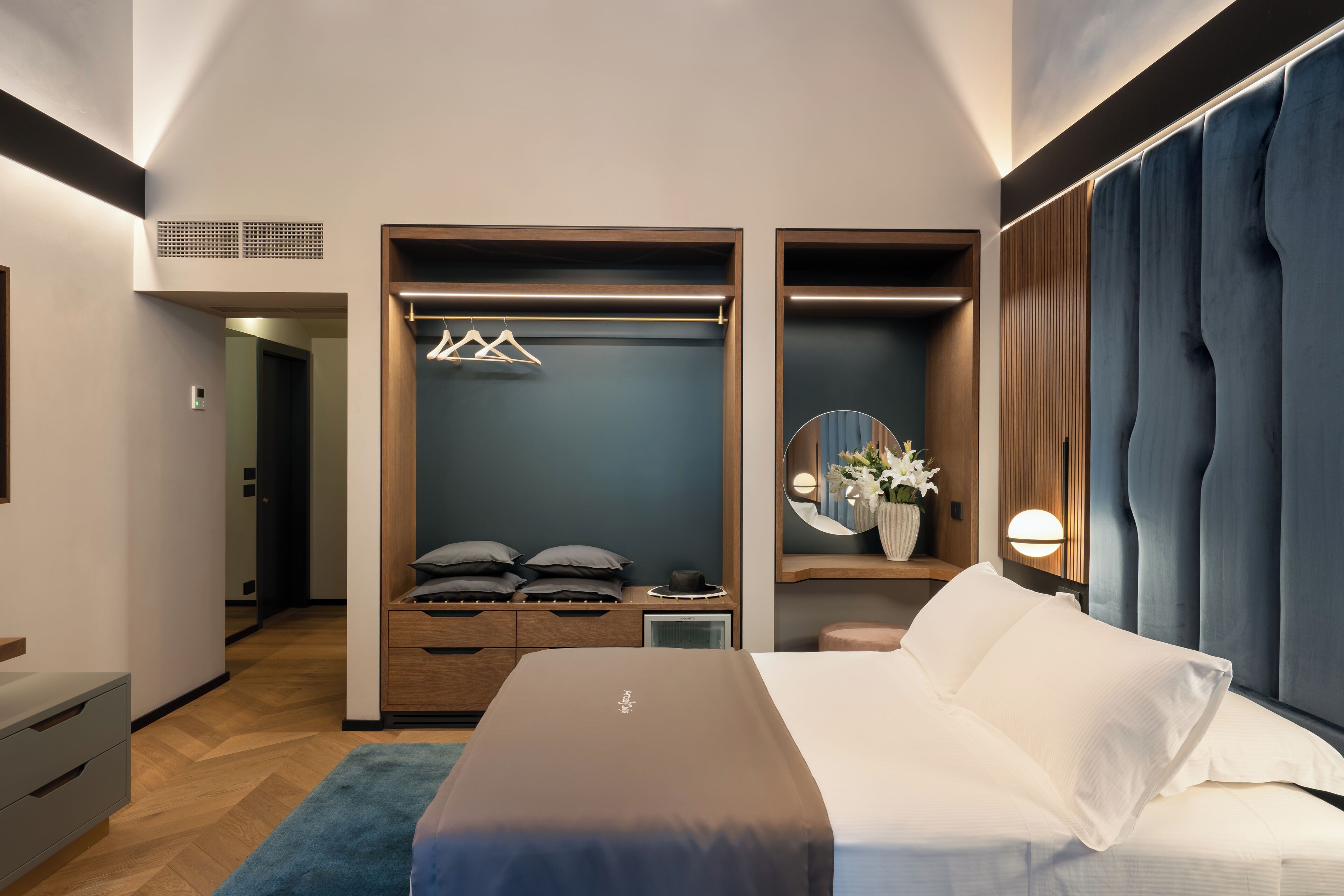 A modern hotel room with a large bed, a walk-in closet, and a vanity area.
