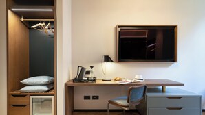 Ein modernes Schlafzimmer mit Einbauschrank, Schreibtisch mit Stuhl, Bett und Nachttisch mit Lampe und Kaffeemaschine.