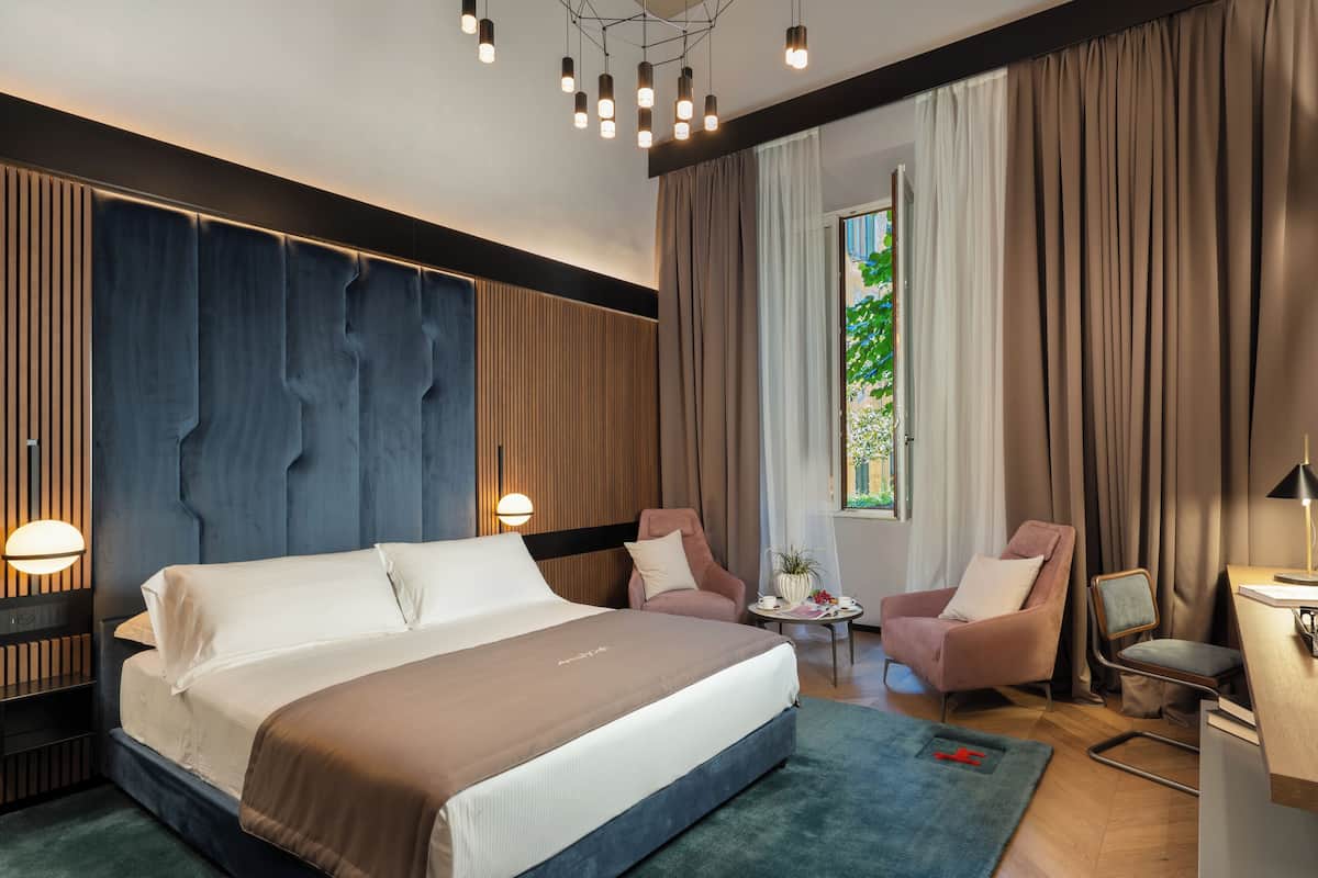 Een moderne hotelkamer met een groot bed, twee fauteuils, een tafeltje en een bureau.
