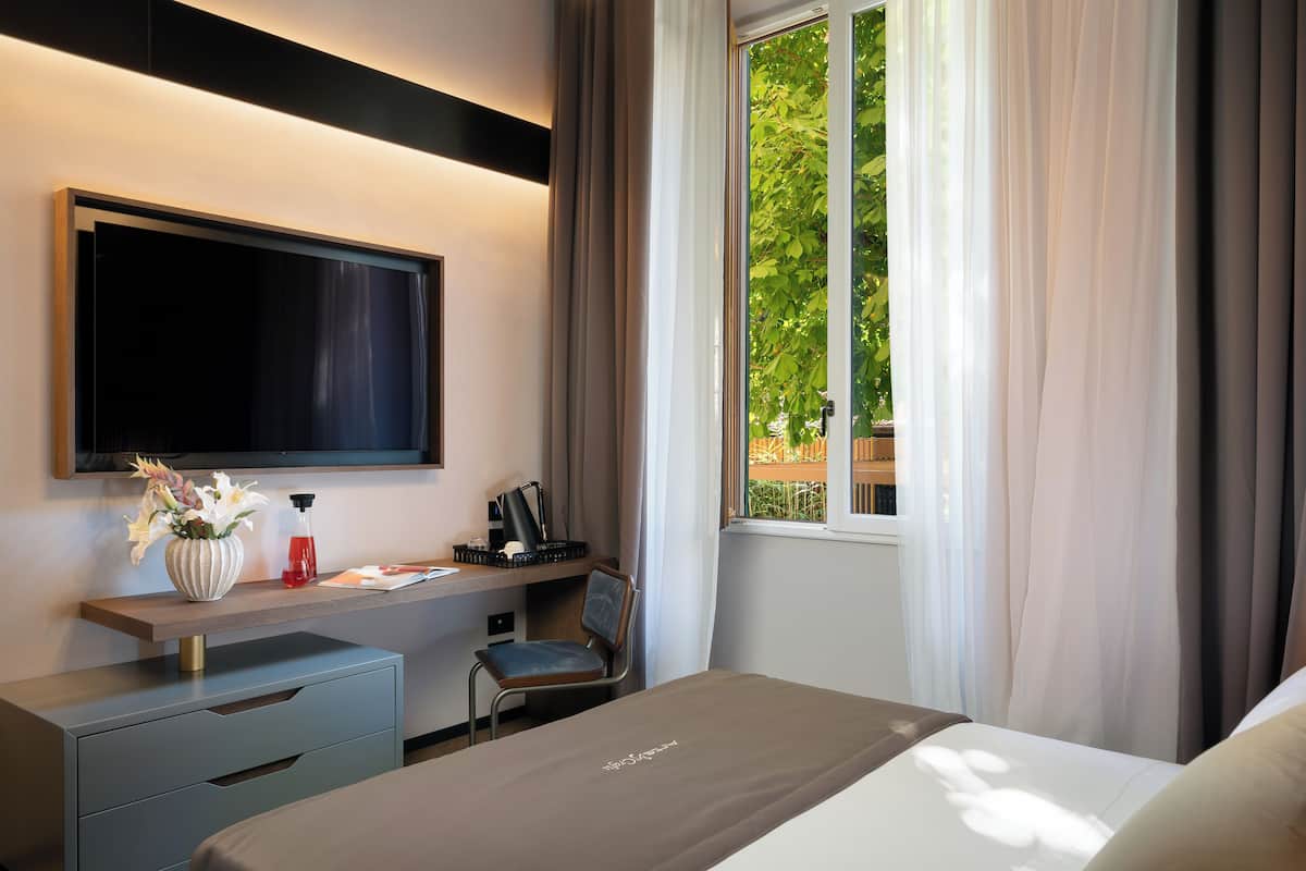 Een hotelkamer met een bed, een bureau met stoel, een televisie en een raam met gordijnen.