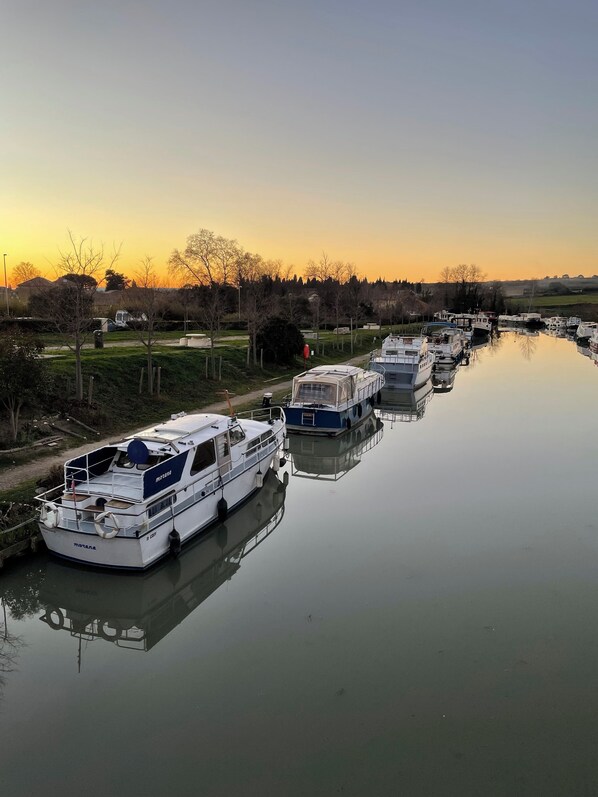 A row of boats docked at a calm water body, likely a canal or river, with a sunset in the background. - Charming atypical gîte, canal du midi, near sea, Capestang center (Capestang)