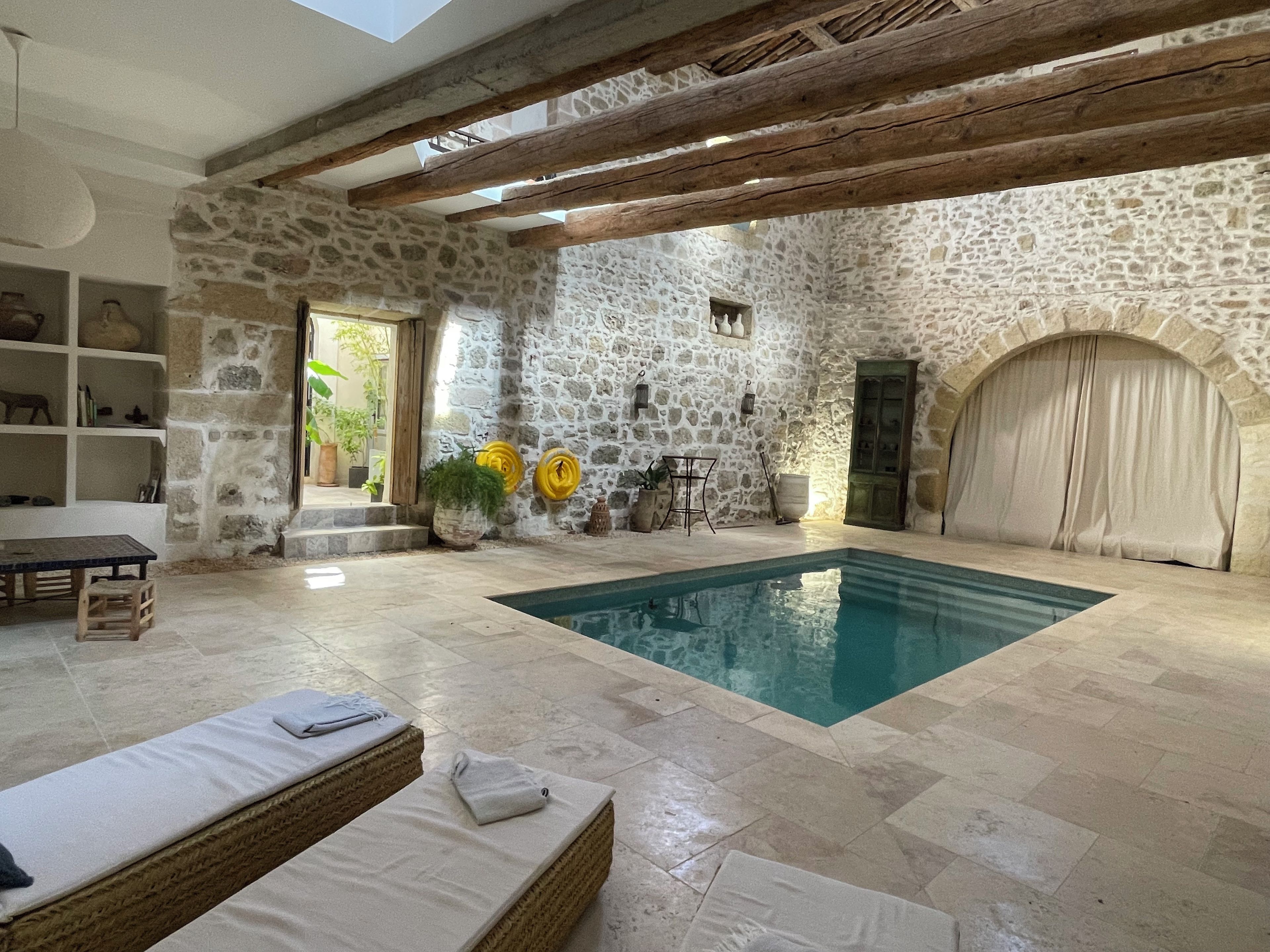 Habitació de pedra amb piscina, bigues de fusta i una banca.