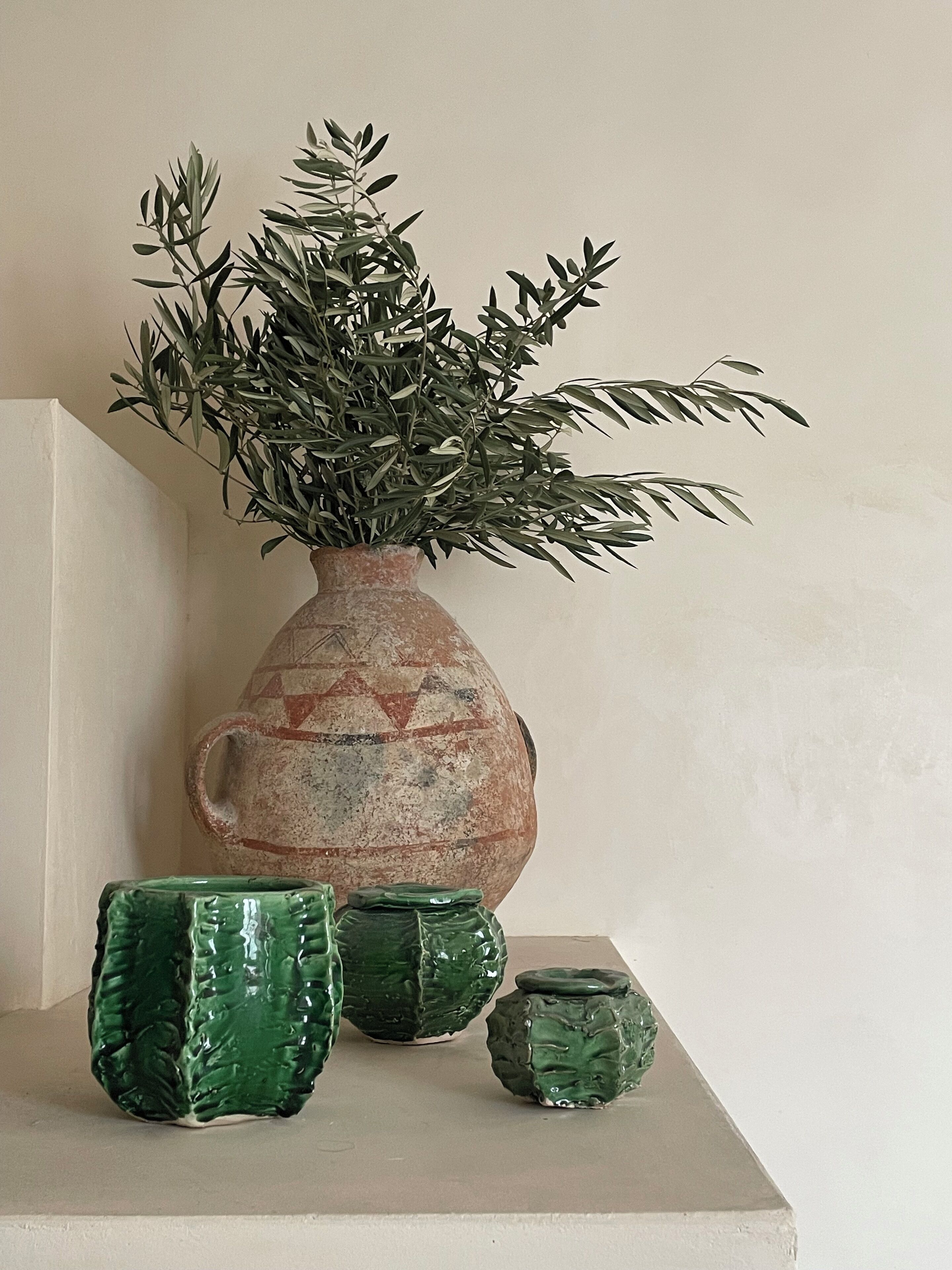 A vase with a plant and three green ceramic containers on a shelf.
