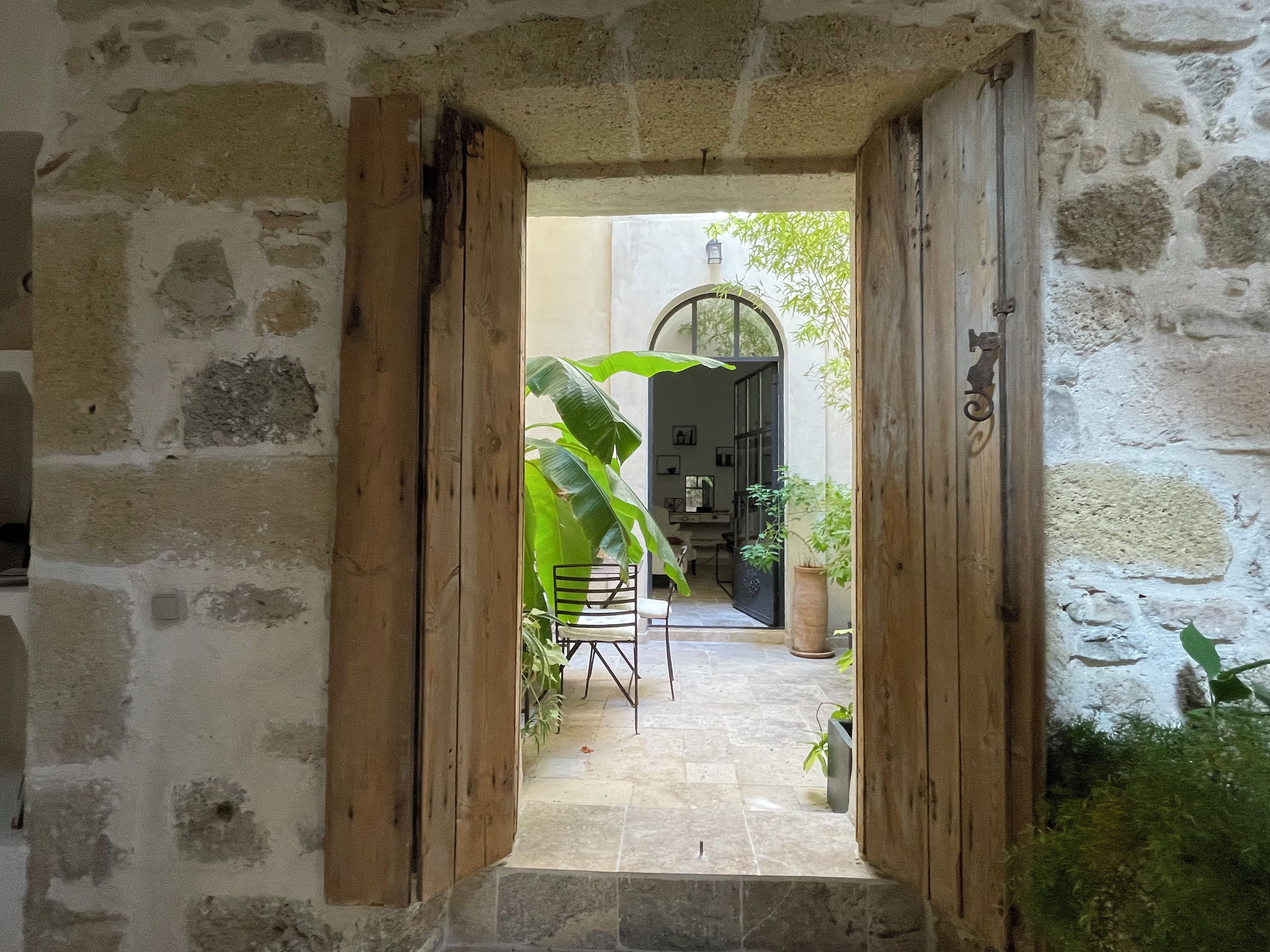 A stone corridor with wooden doors leading to a room with a tiled floor and a chair.