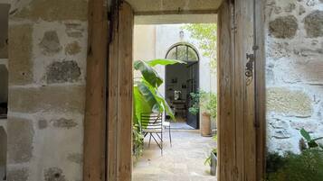 A stone corridor with wooden doors leading to a room with a tiled floor and a chair.