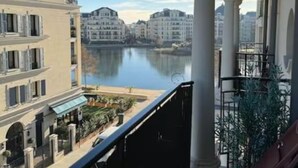 Uma varanda com vista para um corpo d'água calmo e edifícios ao fundo.