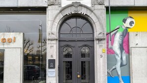 Ein Gebäude mit einer schwarzen Doppeltür, mit den Nummern 8 und 9, und einem farbenfrohen Wandbild auf der rechten Seite.