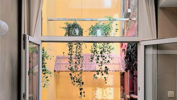 Une pièce dotée d’une porte-fenêtre coulissante donnant sur une petite cour intérieure, où se trouvent une table, des chaises, un pot de fleurs et d’où l’on peut admirer la rue.
