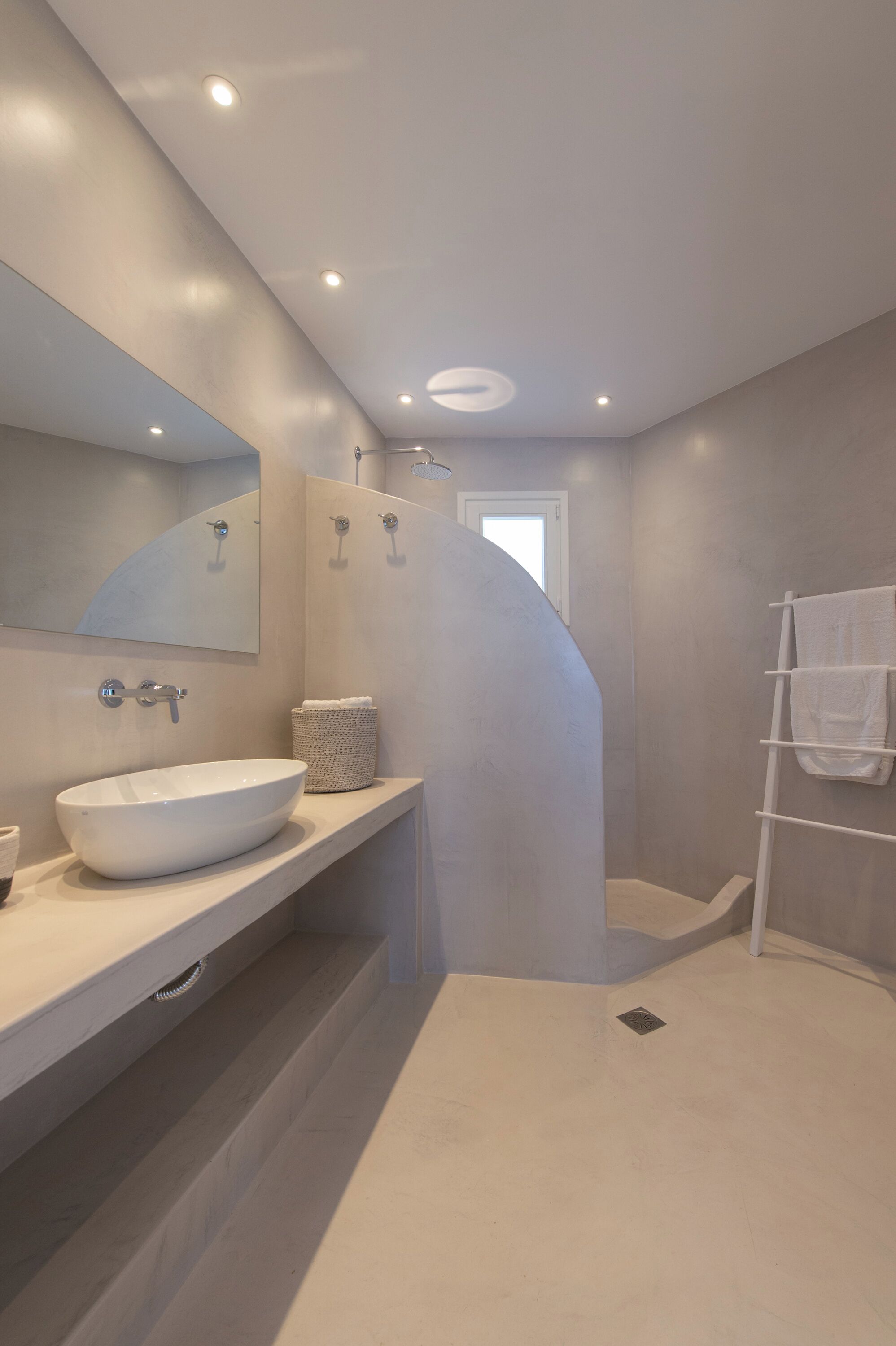 Un baño moderno con un lavamanos ovalado grande, un espejo, un perchero para toallas y una zona de ducha.
