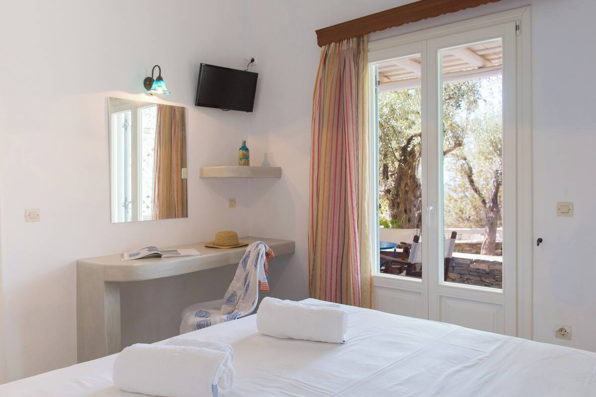 Une chambre d’hôtel équipée d’un lit, d’un meuble-lavabo, d’un téléviseur fixé au mur et d’une fenêtre avec des rideaux.