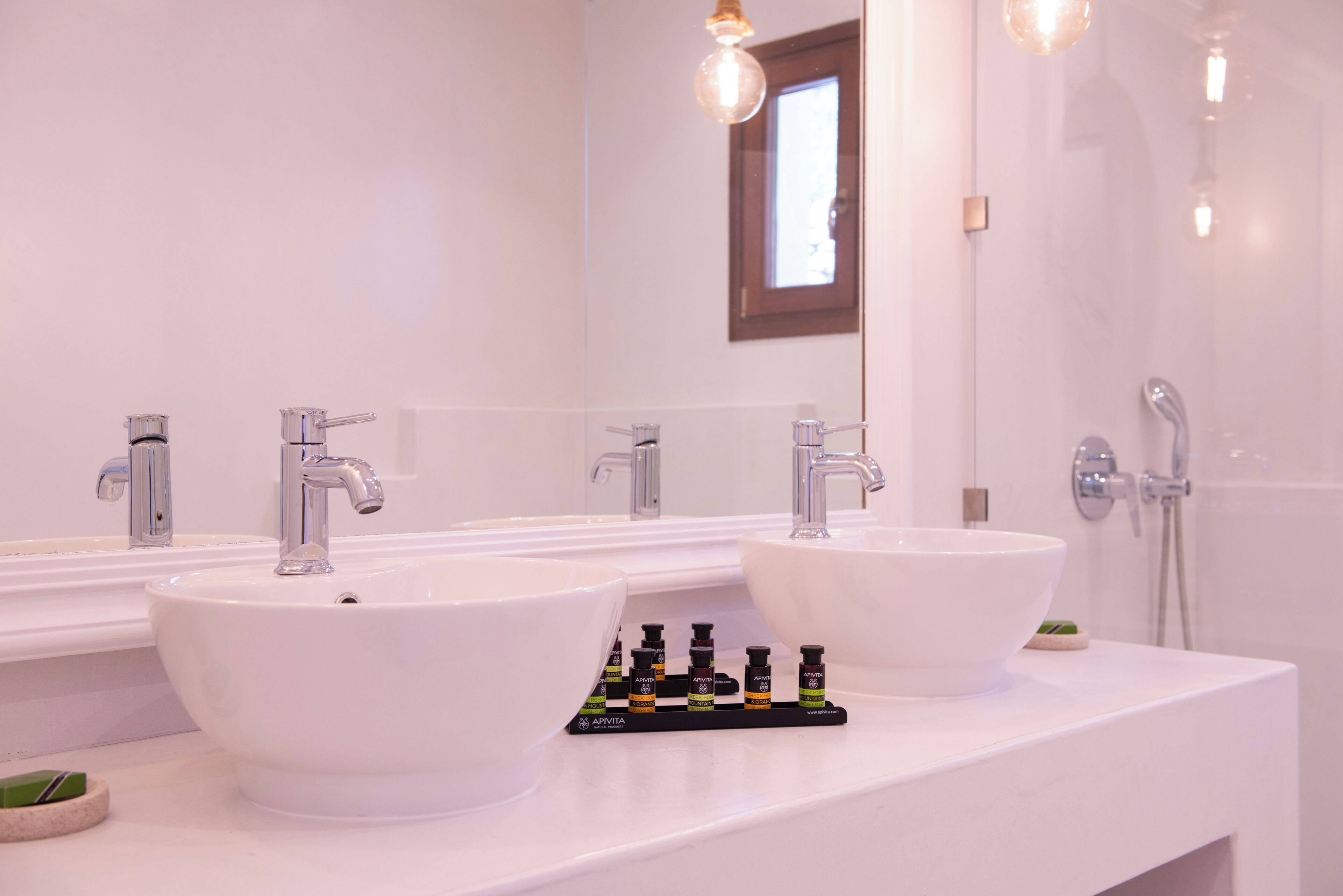 A bathroom with two white sinks, a mirror, and a shower.