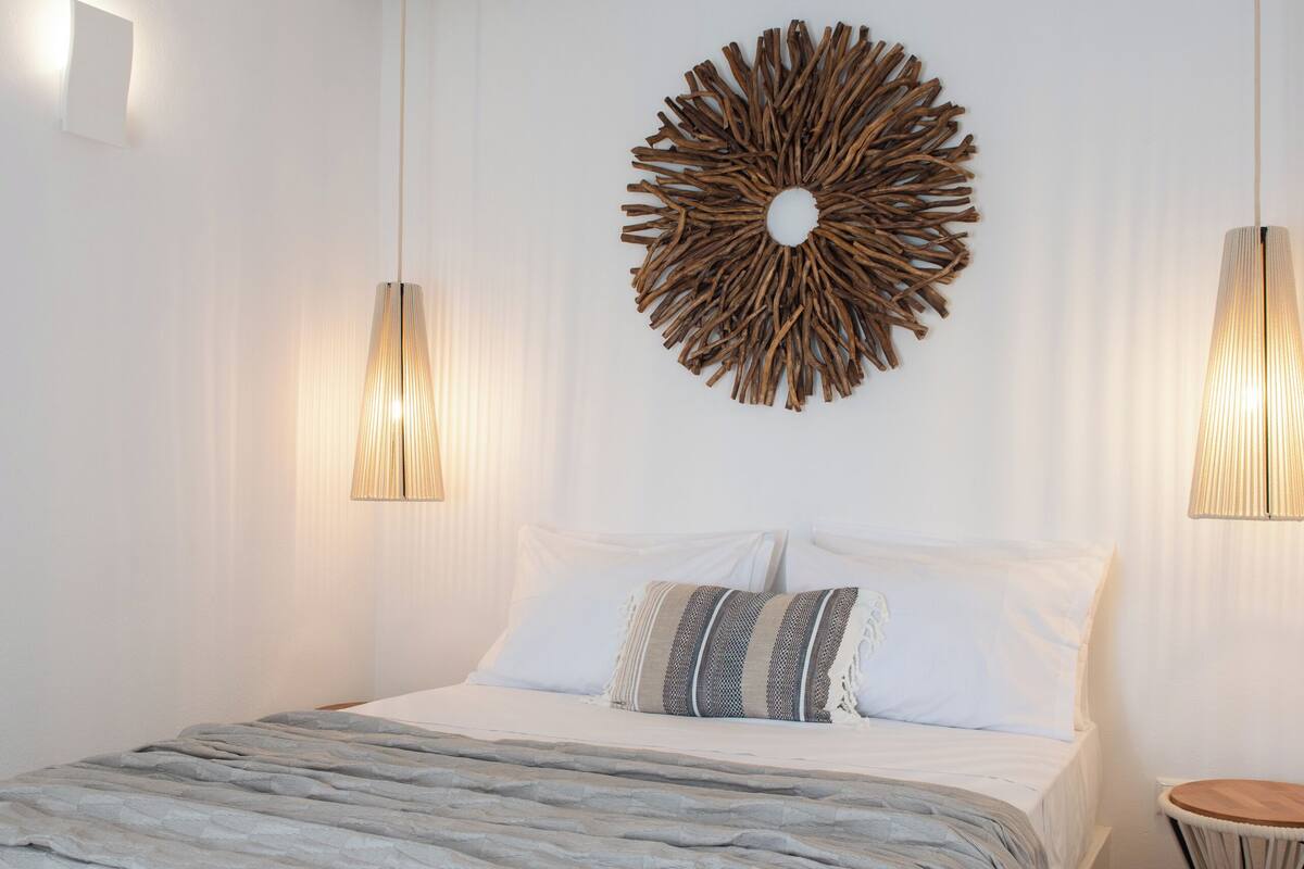 Une chambre à coucher avec un lit, deux lampes fixées au mur, un élément de décoration circulaire accroché au mur et une petite table ronde.