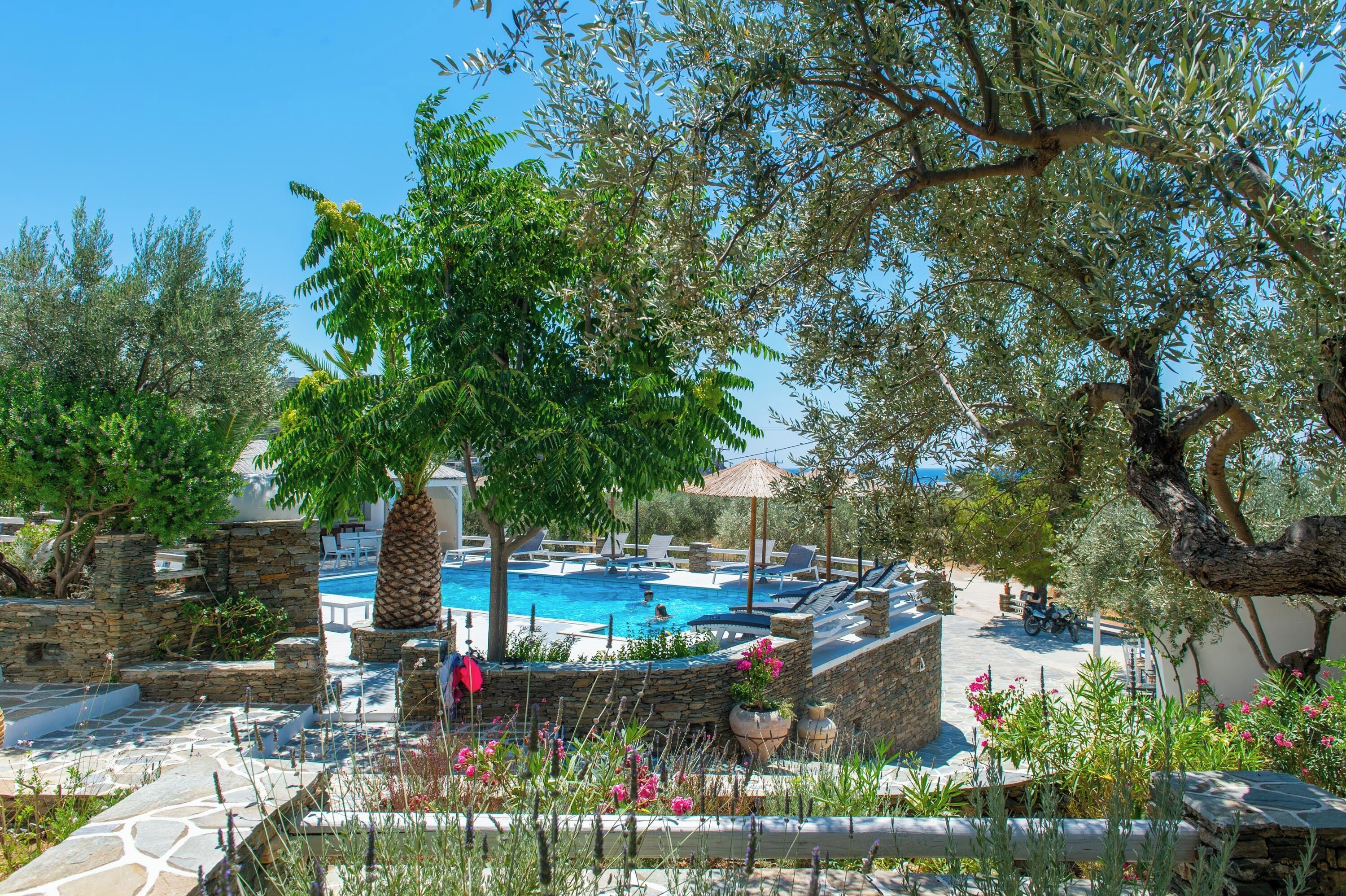 A pool area with stone walls, lounge chairs, and a tree providing shade.