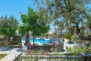 A pool area with stone walls, lounge chairs, and a tree providing shade. - Villa Irini Sifnos (Sifnos)