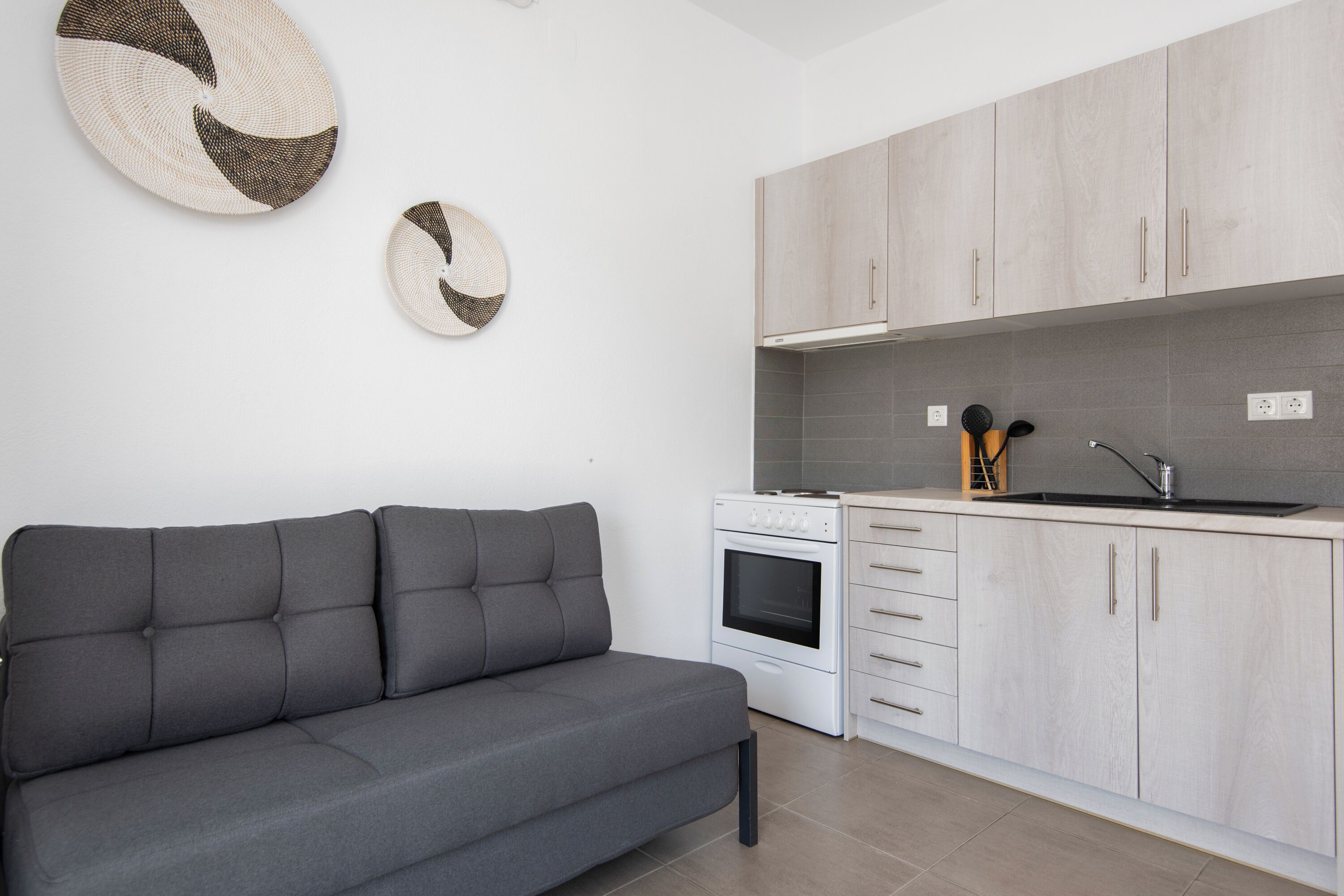 A modern kitchen with grey cabinets, a white stove, and a grey sofa.