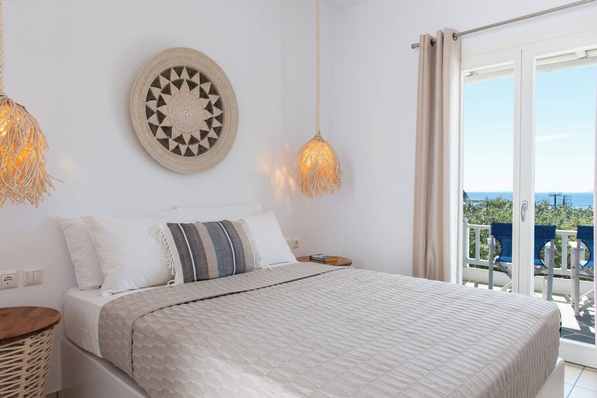 Une chambre à coucher comprenant un lit, des tables de chevet, une décoration murale et un balcon avec des chaises.