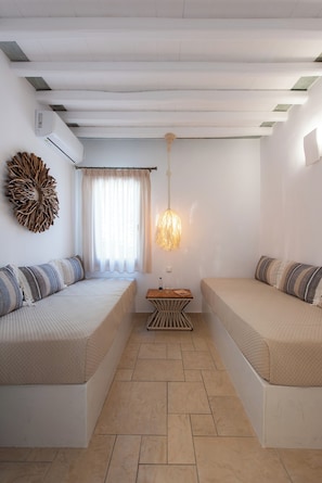A room with two beds, a ceiling fan, a wall-mounted air conditioner, and a decorative wall piece. - Villa Irini Sifnos (Sifnos)