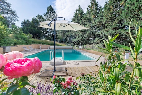 A swimming pool with a wooden deck, surrounded by lush greenery and a large umbrella.. Maison des hôtes – Dordogne: Charming Cottage for 4-5 Guests in Nature