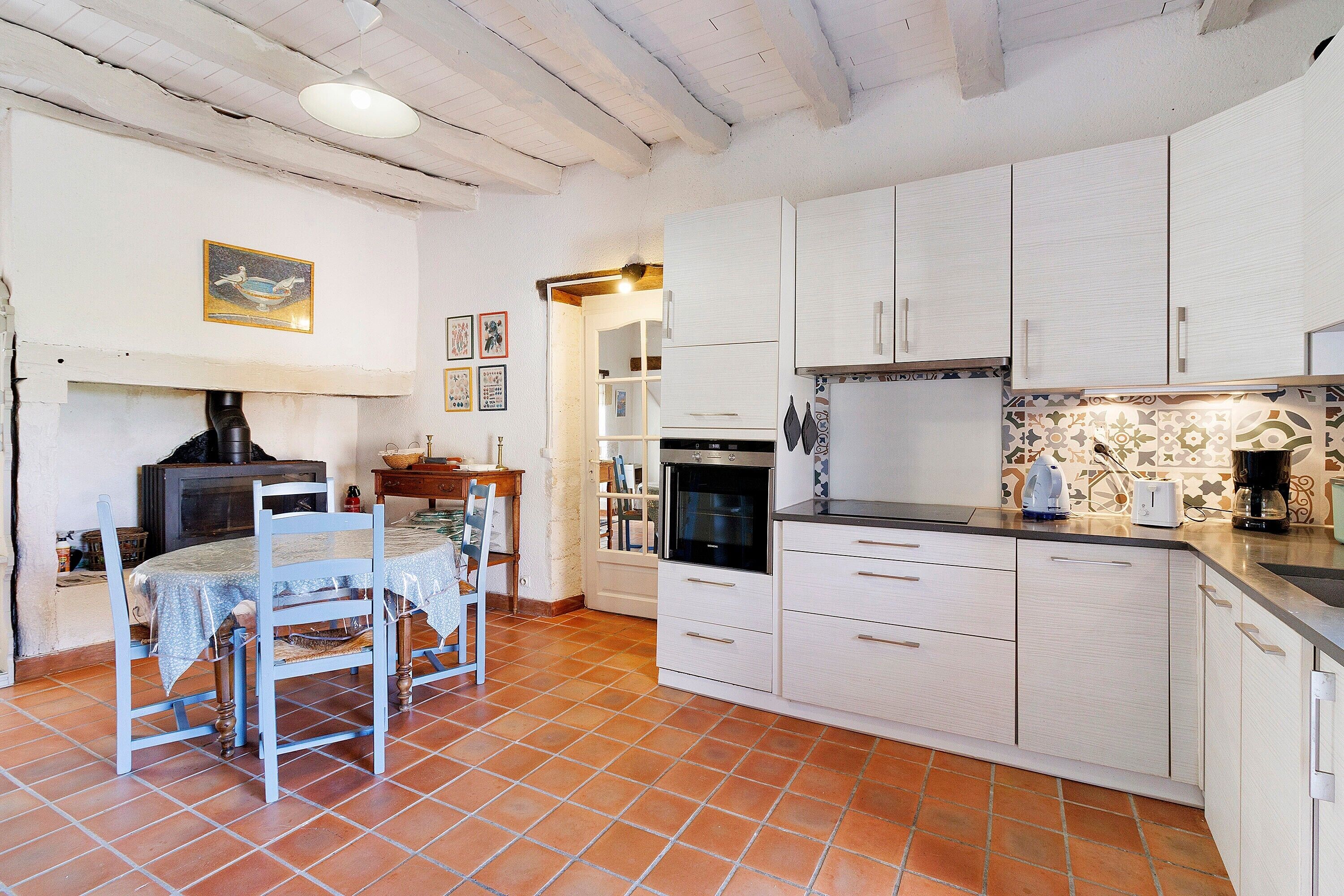 A kitchen with white cabinets, a dining table with chairs, and a tiled floor.