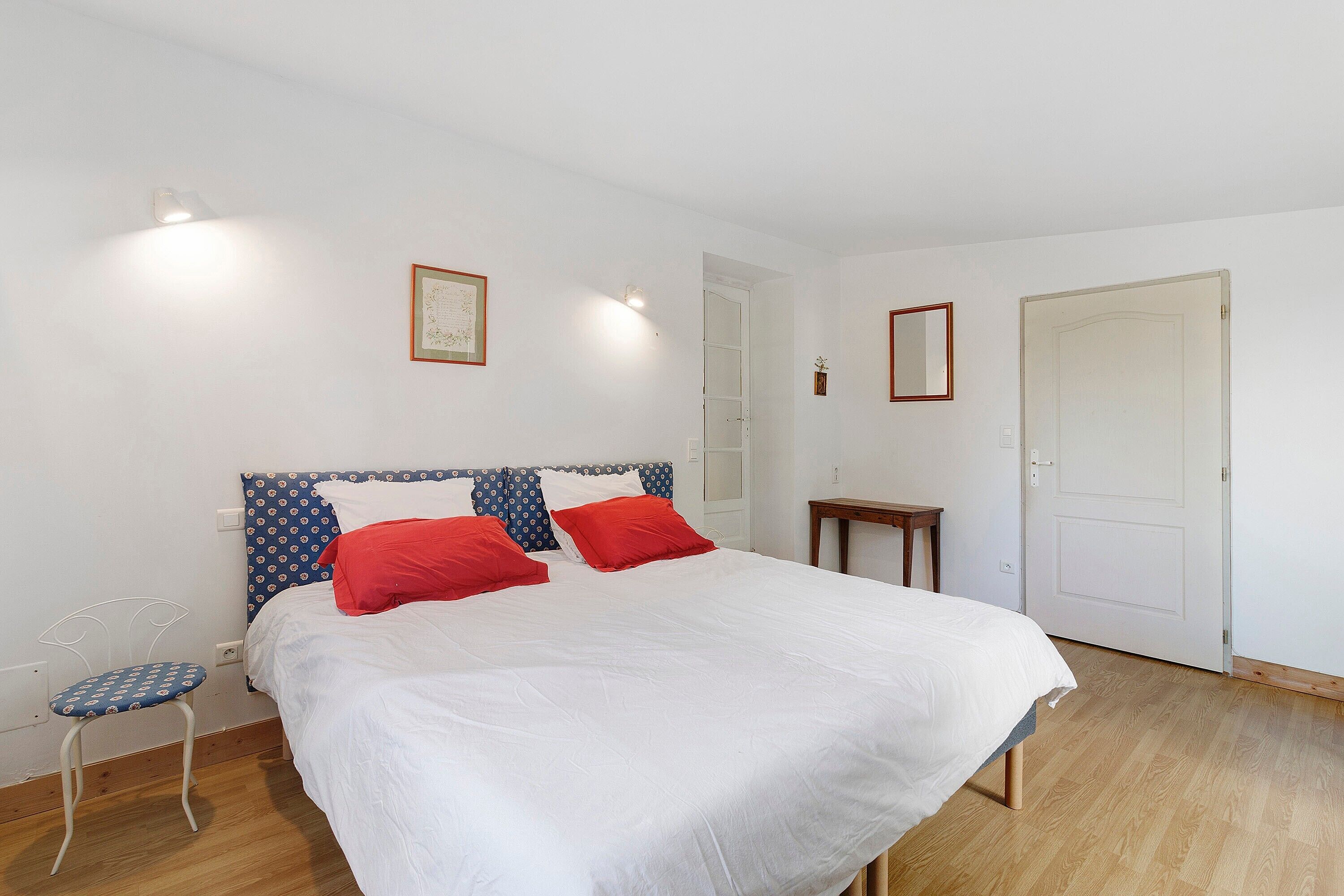 A bedroom with a bed, a chair, a door, and a small table.
