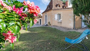 A house with a lawn, a blue chair, and pink flowers. - Maison des hôtes – Dordogne: Charming Cottage for 4-5 Guests in Nature (Saint-Crépin-d'Auberoche)